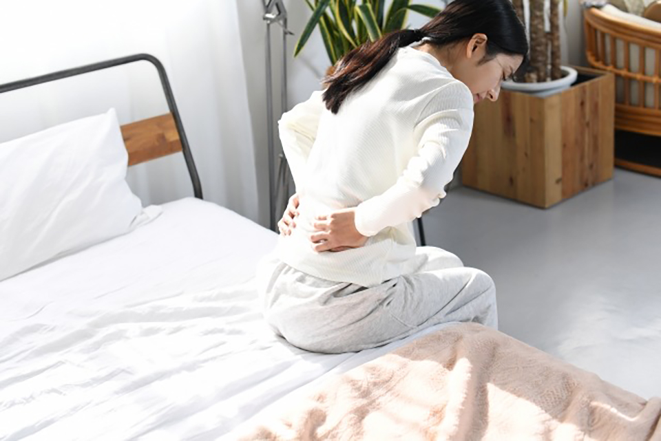 秋の気温変化により起床時に腰の不調を感じる女性のイメージ