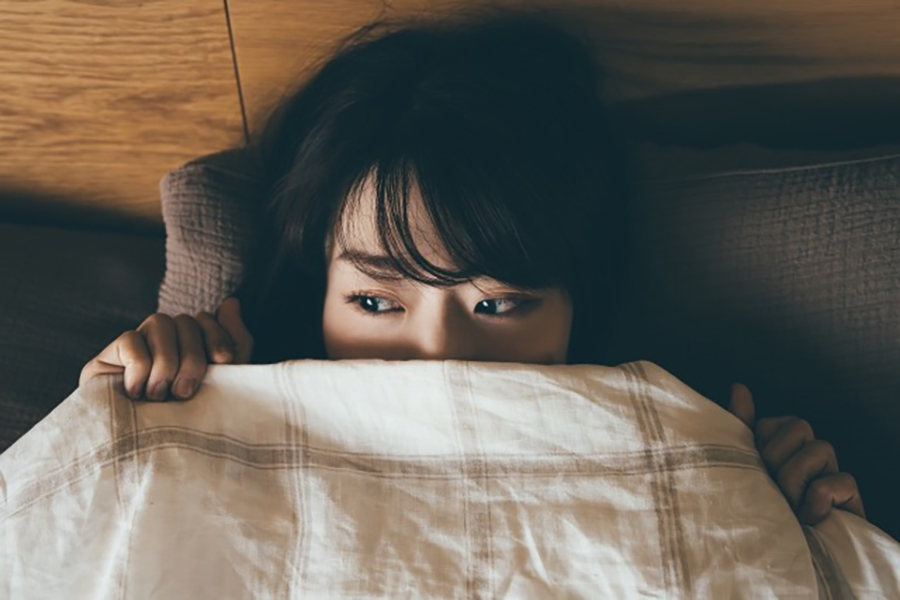 「季節性のメンタル不調」によりベッドで眠れず悩む女性のイメージ